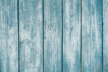 Vertical old wooden boards are painted in a dark cyan color. The paint is weathered and washed away by water. The roughness and structure of the wood are visible