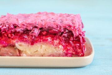 Traditional Russian Salad Herring Under The Fur made of salty herring, boiled potato, beetroot, mayonnaise on ceramic platter for New Year, Winter holidays.
