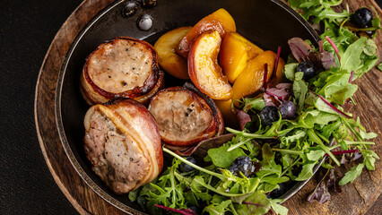 Pork medallions wrapped in bacon with salad and peaches.