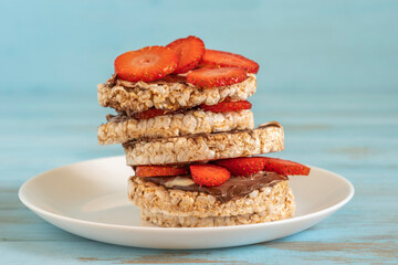 Sandwich made of rice cakes, fresh strawberries and chocolate and nut butter on ceramic plate.
