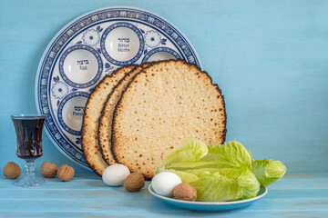 Jewish holiday Pesach or Passover concept with symbolic food (eggs, walnuts, lettuce leaves, matzah) on the background of traditional Seder Plate and blue wood background.