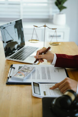 A professional reviews legal and financial documents, using a calculator, money stack, and laptop beside justice scales in office.