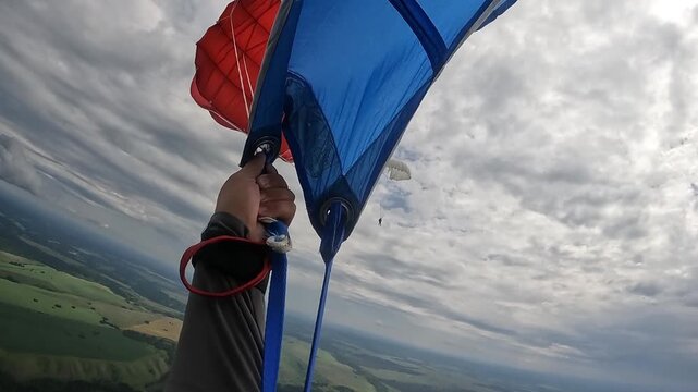 A close&mdash;up focusing on a skydiver performing a dome jump next to colorful parachutes over a heterogeneous agricultural area and an impressive sky - perfect for skydiving, training and adventure.