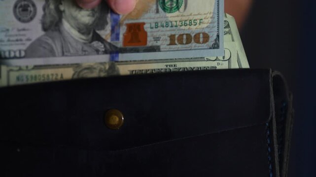 A man pays at a bank and takes money out of his wallet.
Storing cash in a wallet.
A man with an open wallet containing a large amount of money.
A wealthy man with dollars in his wallet.
