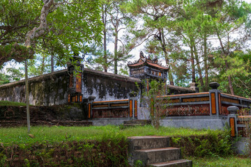 A secluded, ornate tomb entrance at Tu Duc's mausoleum in Hue, Vietnam, framed by lush greenery and towering pine trees.