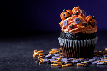 Halloween cupcakes with Halloween sprinkles on black surface and purple background. Copy space