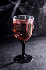 Halloween spooky red cocktail in skeleton hand glass on black background
