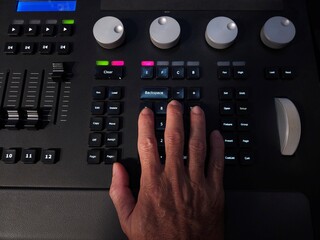 A person operating a professional lighting console panel with one hand, adjusting buttons in a studio or live event setting.