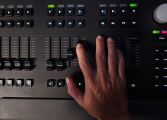 A person operating a professional lighting console panel with one hand, adjusting buttons in a studio or live event setting.