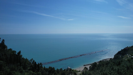 Scenic aerial view of the Adriatic Sea coastline and beach in Numana Le Marche Italy featuring a breakwater and lush green foliage under a clear blue sky