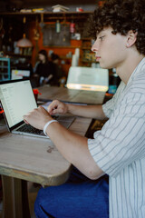 A young man focused on his laptop in a quaint cafe, demonstrating productivity during the afternoon. The warm atmosphere and casual decor create an inviting workspace for creativity.