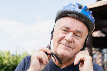 Senior man wearing a blue bicycle helmet outdoors, adjusting the straps before cycling.