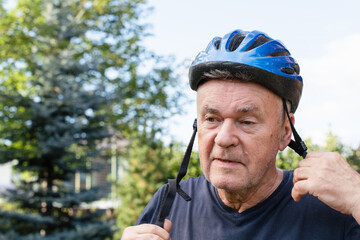 Senior man wearing a blue bicycle helmet outdoors, adjusting the straps before cycling.