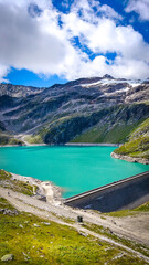 Austria, 08-2025 : wide shot of Weißsee reservoir lake, mountains and glaciers in background. People walking on the dam are visible.