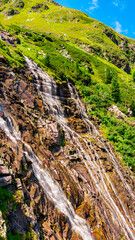 Austria, 08-2025 : water flowing down a mountain, near the weißsee lake. Green grass and blue sky in background.