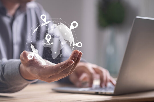 Businessman using laptop with digital hologram globe and location pins, representing global business, GPS navigation, worldwide connection, online communication, and network technology concept.