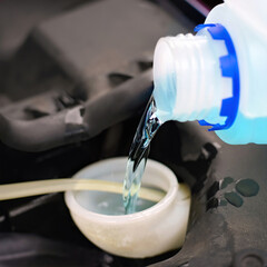 Close up view of car windshield washer tank being refilled with blue cleaning deicing solution during cold season, automotive service and safety preparation. Selective focus