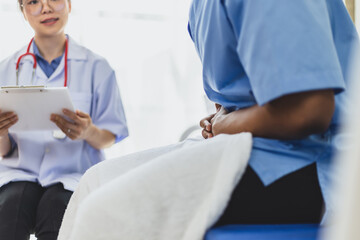A female doctor talks to a young Asian woman about her stomach pain at the clinic table.