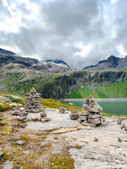 Austria, 08-2025 : Cairns in foreground, weißsee lake, moutains and a cloudy sky in background.
