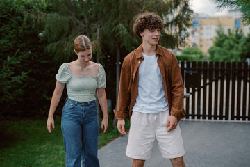 Obraz premium A young couple walks together in a green backyard, with cheerful expressions. The girl wears a light top and high-waisted jeans, while the boy sports a casual outfit.