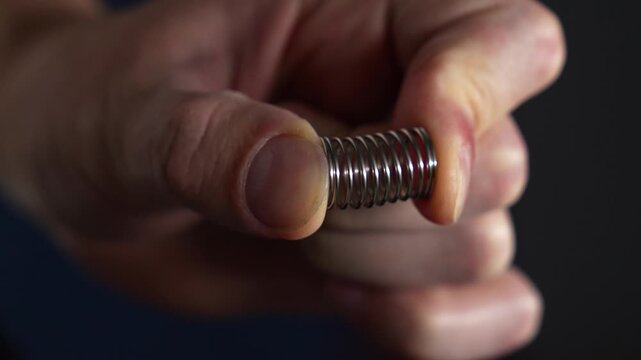 A compressed steel spring in a person's hands.
Pressure on the spring with hands.
A man holds a shock-absorbing spring and compresses it with his fingers.
Spring, pressure, steel, part
