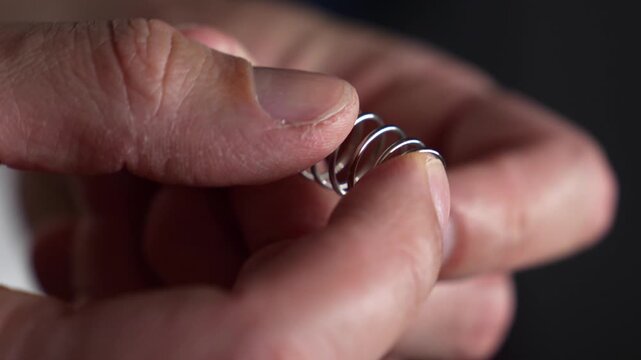 A compressed steel spring in a person's hands.
Pressure on the spring with hands.
A man holds a shock-absorbing spring and compresses it with his fingers.
Spring, pressure, steel, part