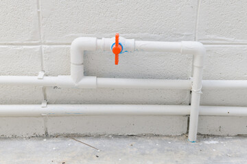 White plumbing pipe detail with an orange valve for water supply during house construction or renovation project. clean and functional system on concrete wall background