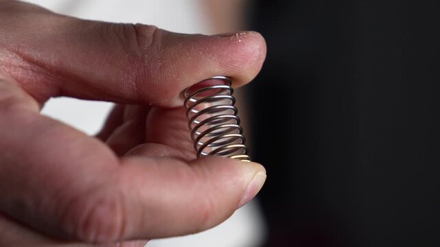 A man compresses a spring with his fingers.
A sturdy metal spring in the hands of a craftsman.
A man compresses a strong metal spring.
Spring, shock absorption, component, macro