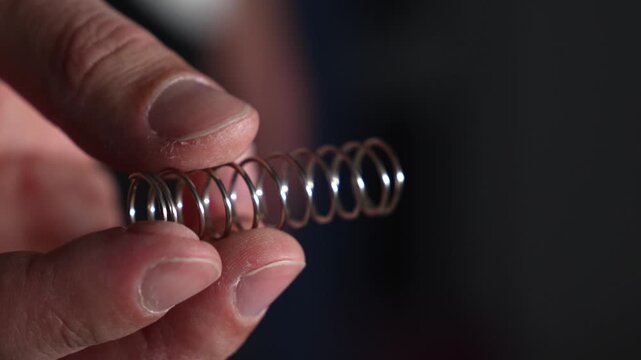 A compressed steel spring in a person's hands.
Pressure on the spring with hands.
A man holds a shock-absorbing spring and compresses it with his fingers.
Spring, pressure, steel, part
