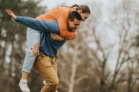 A cheerful moment of a couple sharing a playful piggyback ride outdoors, embodying joy and companionship in a natural, scenic setting surrounded by trees and fresh air. - Powered by Adobe