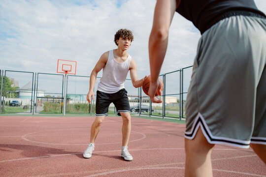 Two young male athletes engage in a competitive basketball game on an outdoor court. The sun shines brightly as they showcase their skills and strategy while dribbling the ball.