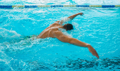 Professional Swimmer Performing Butterfly Stroke &ndash; Speed, Power and Determination. Swimming Competition &ndash; Athlete in Butterfly Style Training in Blue Water Pool