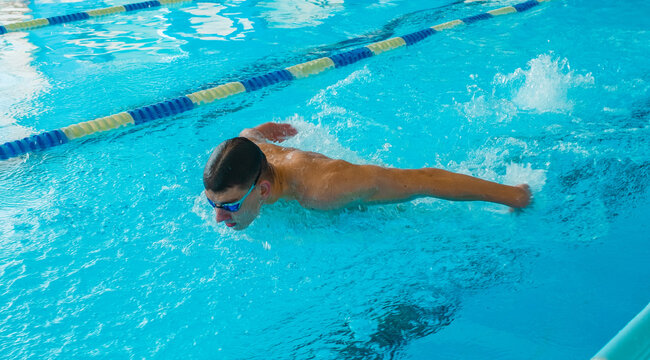 Professional Swimmer Performing Butterfly Stroke &ndash; Speed, Power and Determination. Swimming Competition &ndash; Athlete in Butterfly Style Training in Blue Water Pool