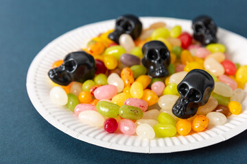 Halloween candy skulls and jelly beans on a white plate on a dark background, close-up
