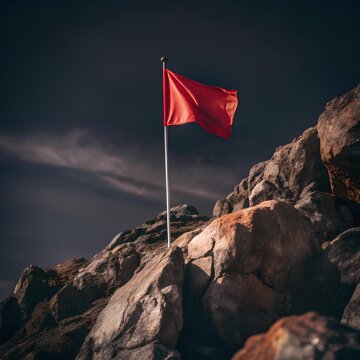 Tattered red flag on thin pole fluttering among rugged rocks under moody sky, evoking symbolism, isolation, and dramatic visual tension
