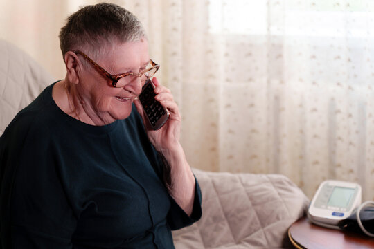 An elderly person utilizes a smartphone while a health monitoring apparatus is placed alongside them, highlighting the embrace of modern conveniences among the older generation.