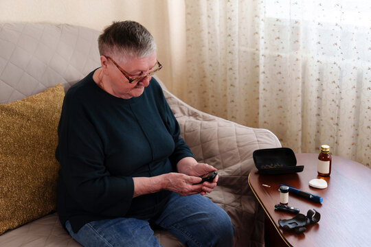 Focused, an elderly woman with short gray hair and glasses uses a glucometer to measure and manage her blood sugar, demonstrating the importance of self-monitoring for her chronic condition.