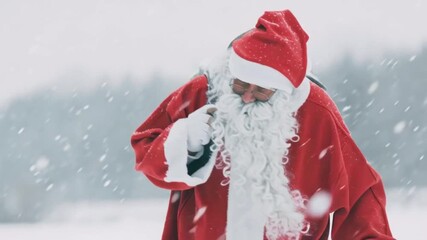 Santa Claus walking in snowy winter forest with gift sack on shoulder, Christmas holiday season festive character in traditional red costume, magical holiday background, New Year celebration atmospher