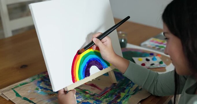 Close up of young female kid painting a rainbow on canvas at home - Hobby, art and creativity concept