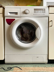 White washing machine stands in a kitchen with wooden cabinets.