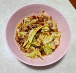 Stir-fried cabbage with oyster sauce and chili, Thai style Stir-fried vegetable and minced pork in pink bowl plate on gray table
