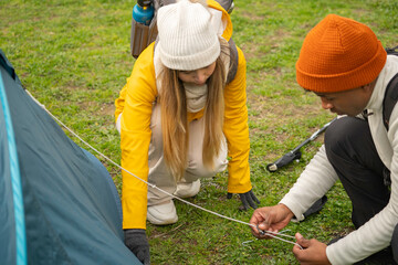 Multiethnic couple of hikers pitching tent on grassy meadow, enjoying outdoor adventure and camping trip