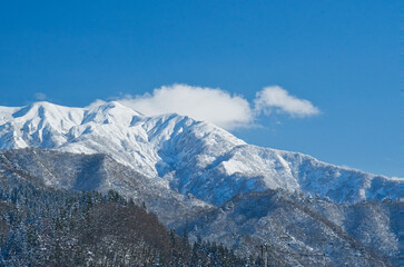 青空の下、白い雲をまとう雪化粧した粟ヶ岳の雄大な姿