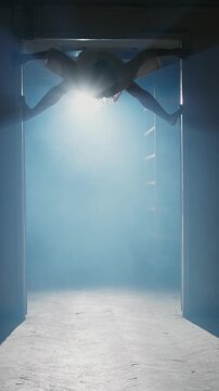 Terrifying silhouette of contortionist girl in hospital gown crawling and jumping in dark corridor with fog and cold backlight creating creepy Halloween horror scene in slow motion