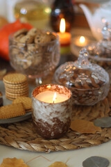 Lit candles, cookies, chocolate, nuts, tea, wine, pumpkins, books, reading glasses and autumn leaves on the table. Autumnal hygge at home. Selective focus.