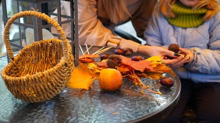 People engaging in creating autumn crafts using fallen leaves, chestnuts, and other natural materials on a table. A wicker basket and lantern add to the cozy seasonal ambiance.