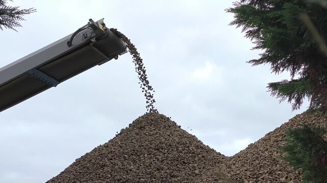 Brita sendo descarregada de uma correia transportadora num monte de cascalho sob um c&eacute;u muito nublado