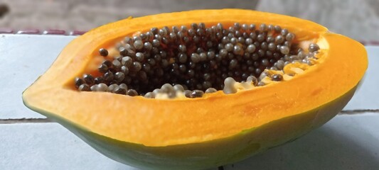 The image shows a ripe papaya fruit that is bright orange in color with a cavity containing many round black seeds, tightly packed together, contrasting with the soft flesh of the fruit.