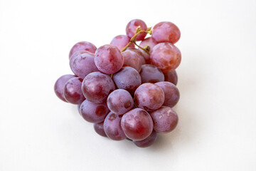 A vibrant bunch of fresh red grapes (Vitis vinifera) is isolated against a white background, perfect for showcasing a healthy and delicious diet.