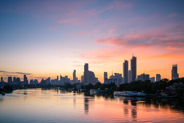 Sunrise skyline view of Bangkok’s Chao Phraya River with high-rise buildings reflecting in the calm morning waters.